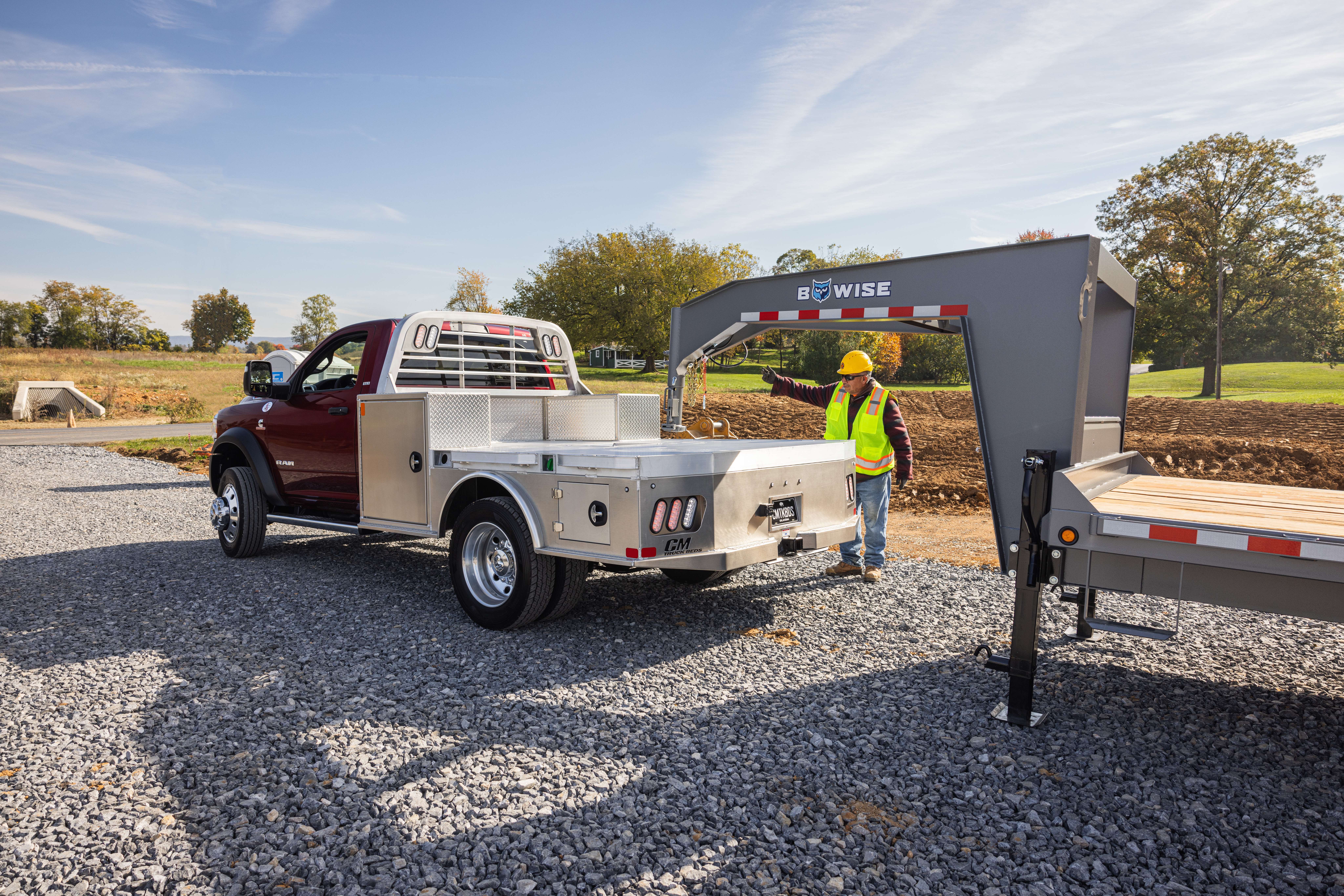 Red pickup truck with aluminum flatbed towing a gooseneck trailer at a construction site.