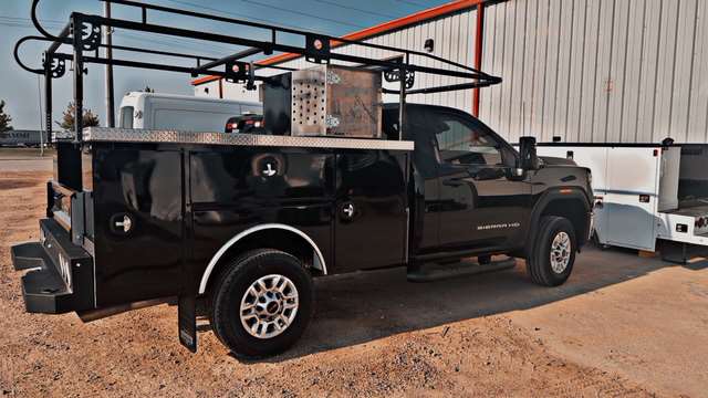 Black GMC Sierra HD service truck with utility body and ladder rack parked outside the CTE Building.