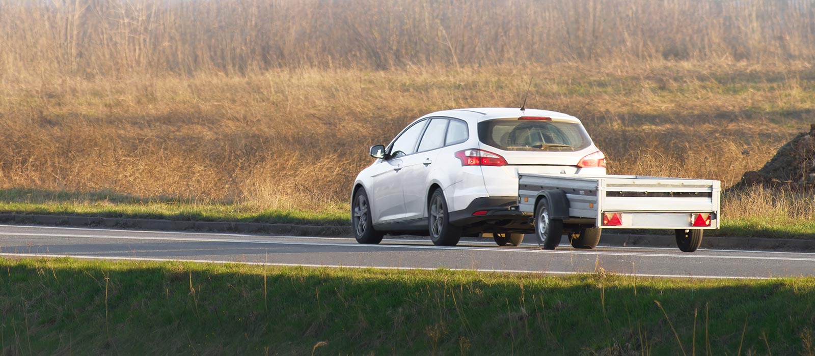 A white crossover hauling a utility trailer by a field.