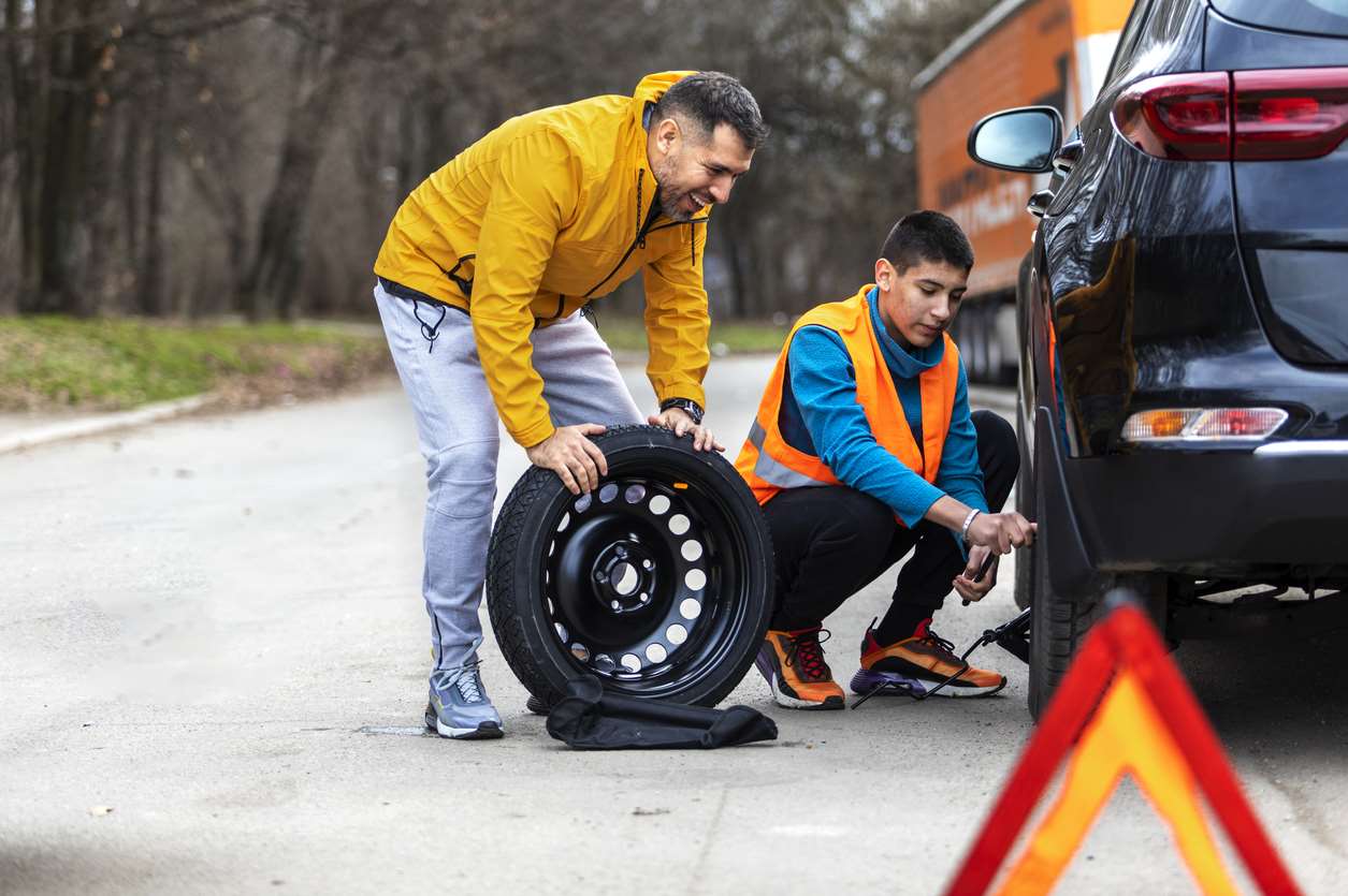 Two men replacing a flat tire with a spare tire.