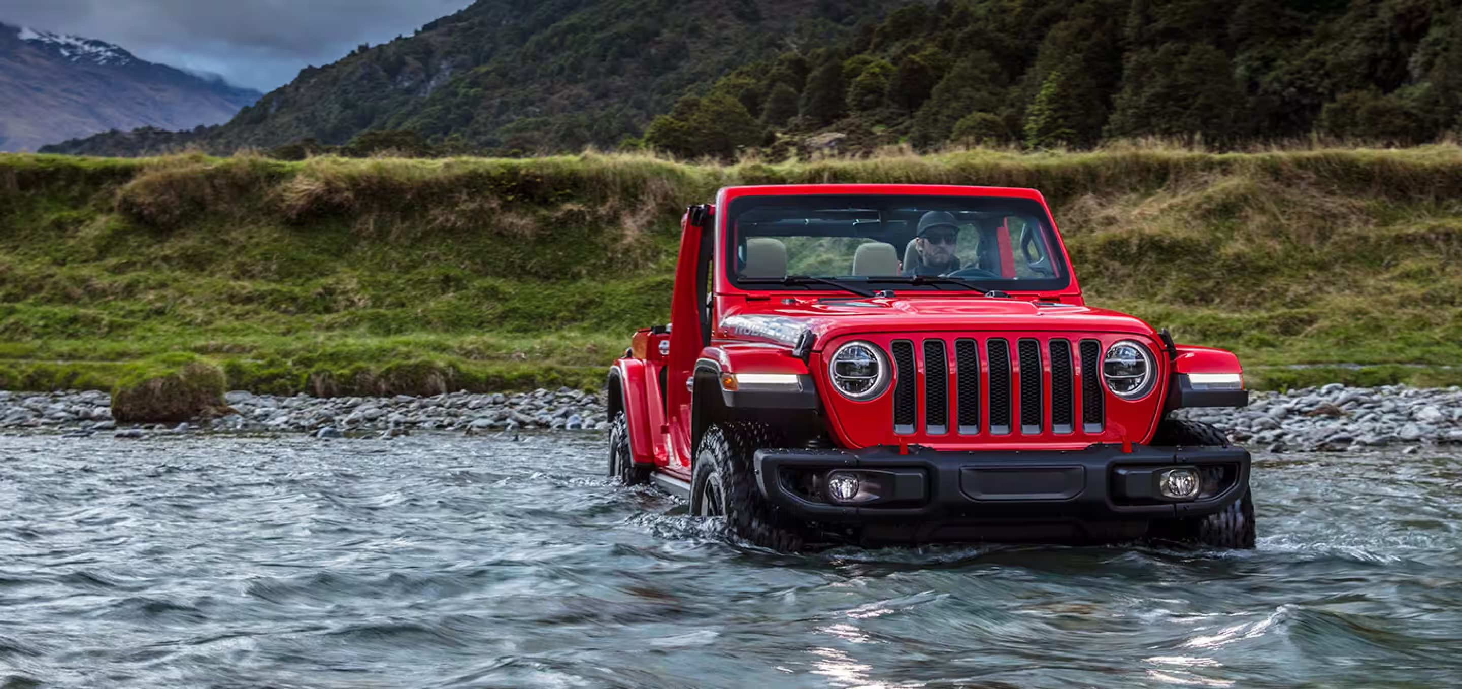 Red Jeep Wrangler fording water in a stream